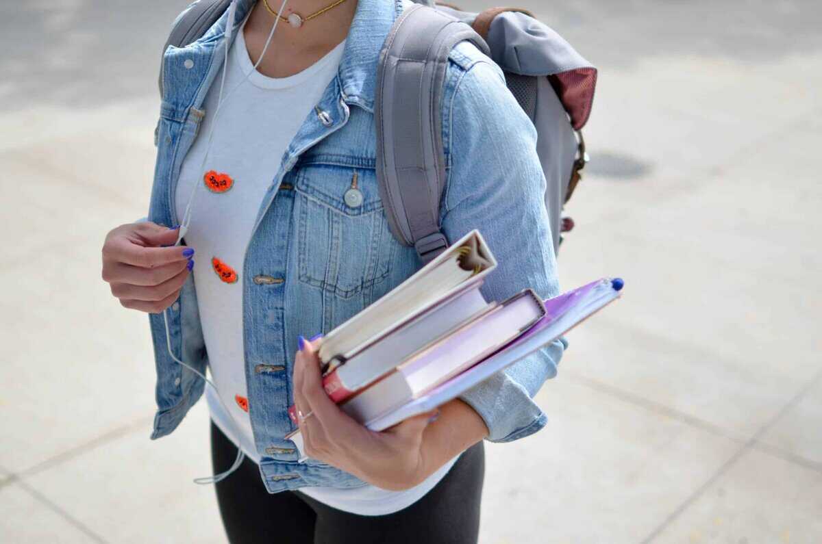 A person wearing a backpack and holding textbooks